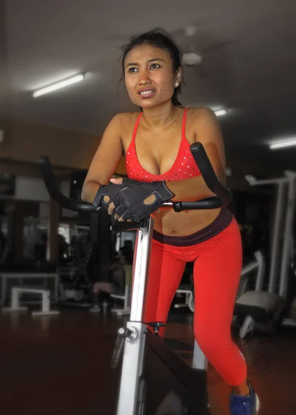 Joven hermosa y sudorosa asiática activa mujer entrenamiento duro ciclismo y montar en bicicleta estática entrenamiento en el gimnasio — Foto de Stock