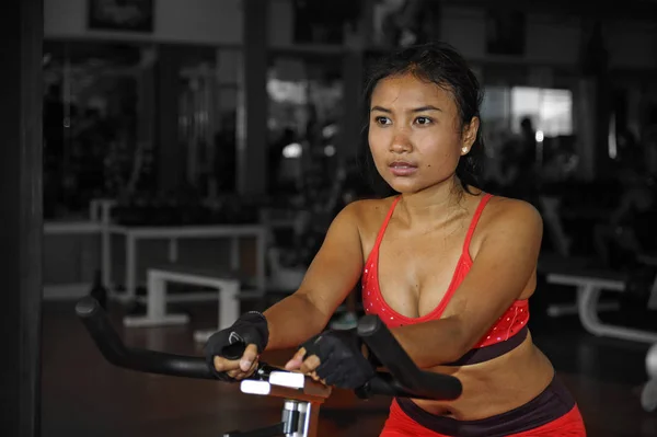 Joven hermosa y sudorosa asiática activa mujer entrenamiento duro ciclismo y montar en bicicleta estática entrenamiento en el gimnasio — Foto de Stock