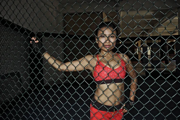 Beautiful and sexy Asian fighter woman in fighting gloves and sport clothes inside MMA cage posing cool — Stock Photo, Image