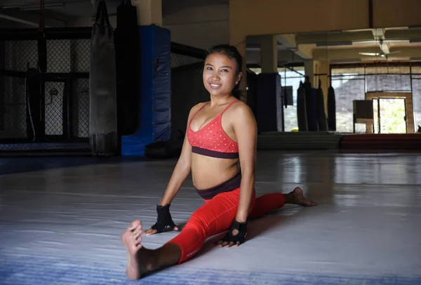 Genç mutlu ve terli Asyalı kadın spor giysiler rahatlamak için germe ve split bacak kasları spor salonu dojo