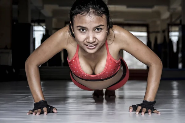 Sexy sudoroso asiático mujer en deporte ropa haciendo flexiones en gimnasio dojo piso sonriendo en duro entrenamiento fitness entrenamiento — Foto de Stock