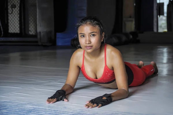 Young beautiful sweaty Asian woman in sport clothes stretching on gym dojo floor smiling posing corporate — Stock Photo, Image