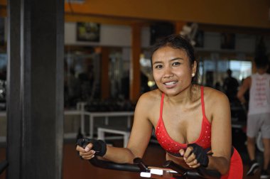 güzel terli Asya mutlu kadın sert Bisiklete binme ve spor salonunda egzersiz statik bisiklet sürme gülümseyen eğitim