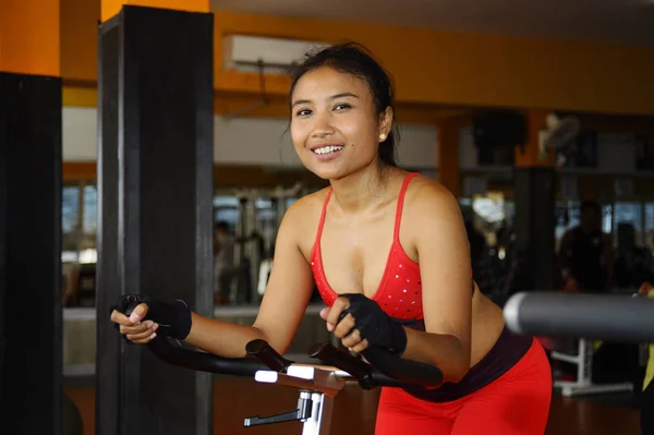 Joven hermosa y sudorosa asiática activa mujer entrenamiento duro ciclismo y montar en bicicleta estática entrenamiento en el gimnasio — Foto de Stock