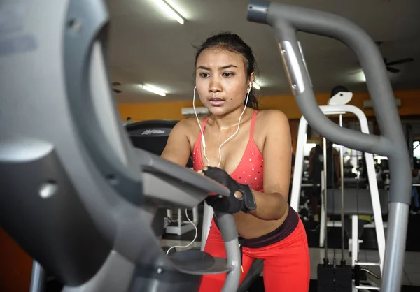 性感和出汗的亚裔女子，在健身房使用椭圆脚踏机齿轮在高强度的锻炼刻苦训练 — 图库照片