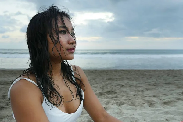 Молодая красивая азиатская девушка с мокрыми волосами на пляже заката, глядя вдаль вдумчивый и задумчивый — стоковое фото