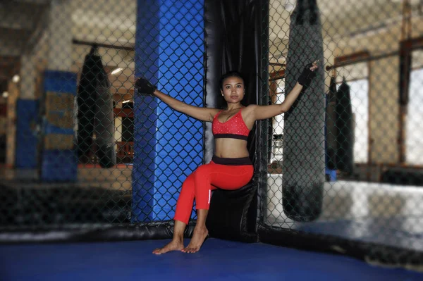 Hermosa y sexy mujer luchadora asiática en guantes de lucha y ropa deportiva dentro de la jaula MMA posando fresco — Foto de Stock