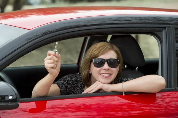 Donna attraente sorridente orgoglioso seduto al sedile del conducente in possesso e mostrando la chiave della macchina in auto nuova acquisto e noleggio — Foto Stock