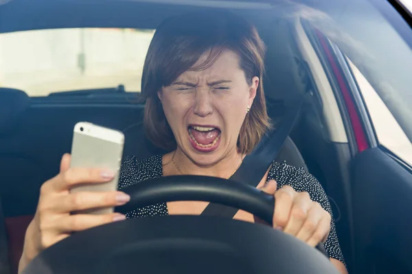 Vacker kvinna kör bil medan textning med hjälp av mobiltelefon distraherad — Stockfoto