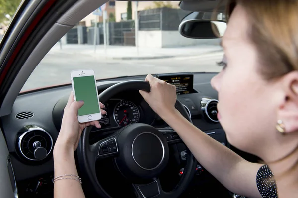 Mano de la mujer sosteniendo el volante y el coche de conducción del teléfono móvil, mientras que los mensajes de texto distraído en riesgo — Foto de Stock