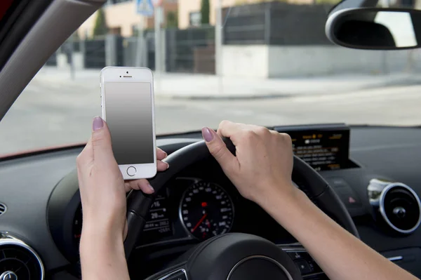 Рука женщины, держащей руль и мобильный телефон за рулем автомобиля, в то время как смс отвлекается на риск — стоковое фото