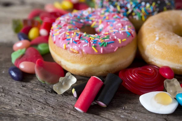 Unhealthy but delicious group of sweet sugar donut cakes and lots of gummy candies on vintage wooden table — Stock Photo, Image