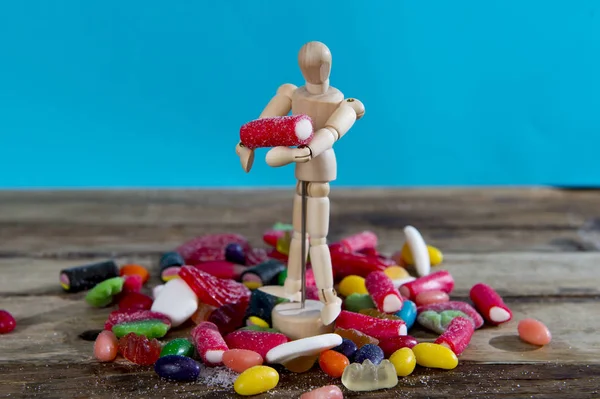 Dummy puppet holding and carrying sweet candy upon pile of licorice and caramel gummies — Stock Photo, Image