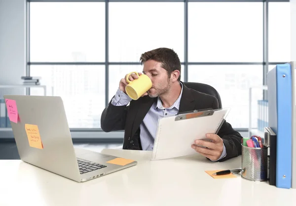 Молодой привлекательный бизнесмен, уверенно работающий в офисе с ноутбуком и бумажной работой — стоковое фото