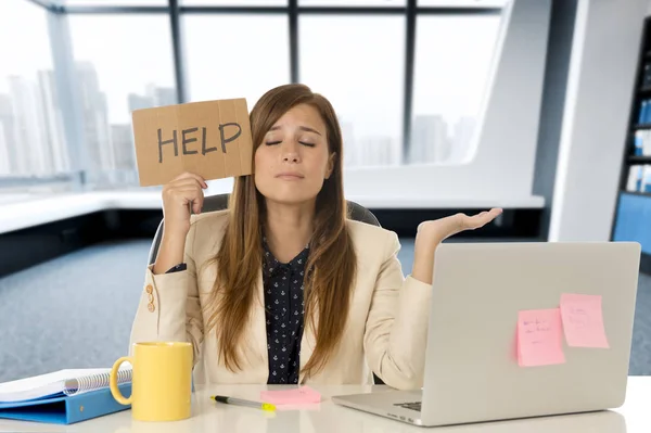 Attraktive, traurige und verzweifelte Geschäftsfrau, die unter Stress am Schreibtisch ihres Bürolaptops leidet und ein Hilfeschild hält — Stockfoto