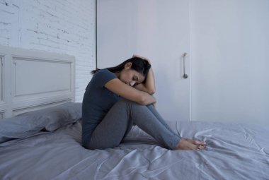 f yatağa evde oturan güzel üzgün ve depresyonda Latin kadın