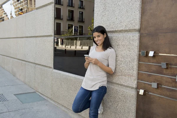 Internet üzerinde cep telefonu mesaj kullanarak kentsel sokak şehir arka plan üzerinde genç güzel ve mutlu latin kadın