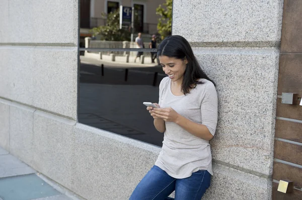 Junge schöne und glückliche lateinische Frau auf städtischen Straße Stadt Hintergrund mit Internet auf Mobiltelefon SMS — Stockfoto