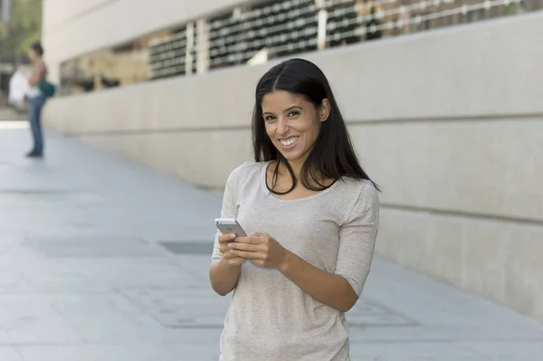 Junge schöne und glückliche lateinische Frau auf städtischen Straße Stadt Hintergrund mit Internet auf Mobiltelefon SMS — Stockfoto