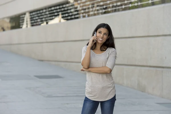 Boldog latin nőt, utcai városi háttér beszélő-ra mozgatható telefon-val egy kedves mosollyal — Stock Fotó