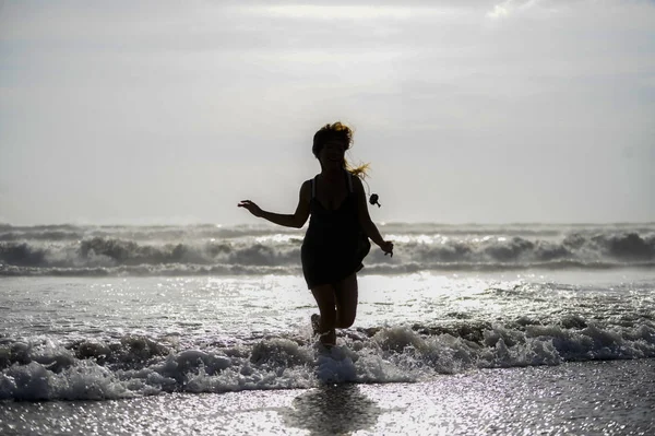 Silhouette of young happy Asian woman relaxed looking at wild sea waves on sunset tropical beach — Stock Photo, Image