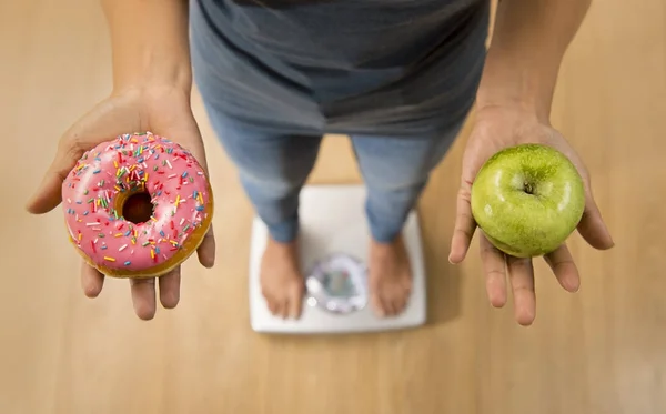 Close-up van de vrouw op gewicht schaal houden in haar apple handfruit en donut als keuze van gezonde versus ongezond voedsel — Stockfoto