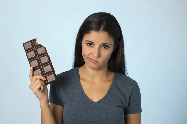 Beautiful latin woman with chocolate bar feeling guilty after biting isolated on blue background in sugar and sweet abuse — Stock Photo, Image
