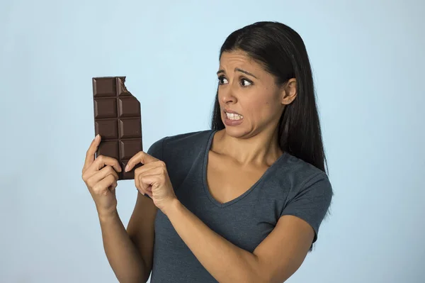 Mooie Latijns-vrouw met chocoladereep schuldgevoel na bijten geïsoleerd op blauwe achtergrond in suiker en zoete misbruik — Stockfoto