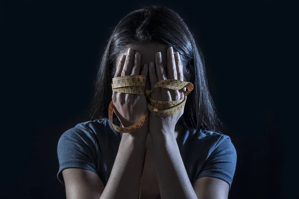 Hände in maßgeschneidertes Maßband gehüllt, das das Gesicht eines jungen depressiven und besorgten Mädchens bedeckt, das an Magersucht oder Bulimie leidet — Stockfoto