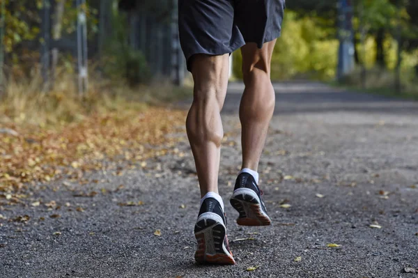 Homem do esporte com pernas atléticas e musculares rasgadas correndo fora da estrada em treino de corrida no campo no fundo Outono — Fotografia de Stock