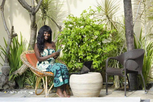 Gelukkig zwarte afro-Amerikaanse vrouw in elegante jurk luxe terras villa met laptop en mobiele telefoon bezig — Stockfoto