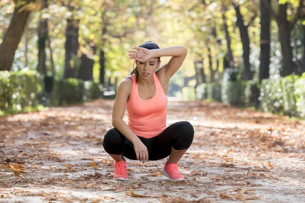 Atractiva mujer deportiva en corredor ropa deportiva respirando jadeando y tomando un descanso cansado y agotado después de correr entrenamiento en el parque de otoño — Foto de Stock