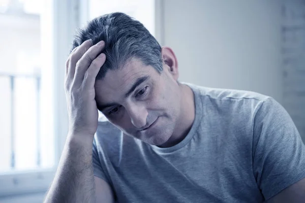 Грустный и обеспокоенный мужчина с седыми волосами сидит дома на диване и смотрит — стоковое фото
