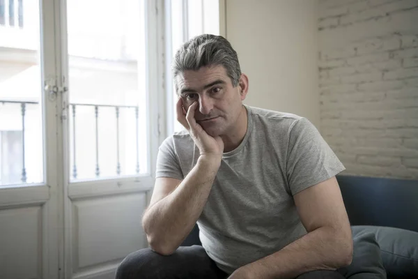 Hombre triste y preocupado con el pelo gris sentado en el sofá de casa buscando — Foto de Stock