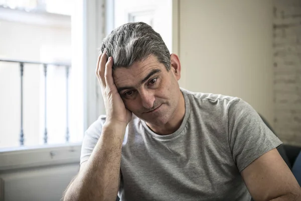 sad and worried man with grey hair sitting at home couch looking