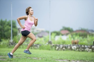 genç çekici Asya spor Çalıştırıcısı kadın fitness konusunda eğitim egzersiz ot arka plan üzerinde mutlu gülümseyerek ormanda çalışan 