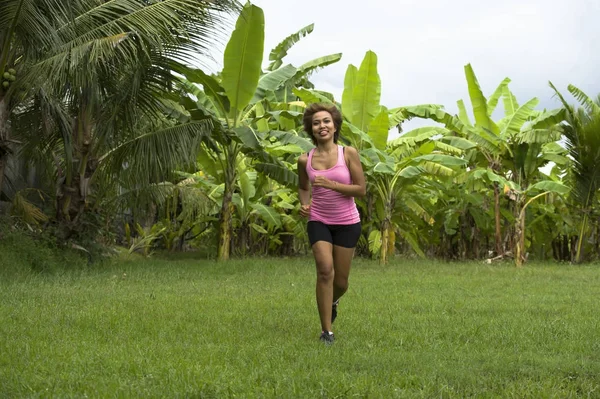Pelari wanita muda Asia yang menarik berlari di hutan tersenyum gembira dalam latihan pada tanaman herbal dengan pohon palem di latar belakang — Stok Foto