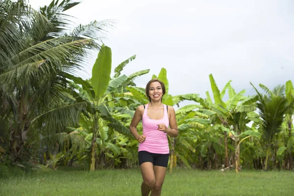 Pelari wanita muda Asia yang menarik berlari di hutan tersenyum gembira dalam latihan pada tanaman herbal dengan pohon palem di latar belakang — Stok Foto