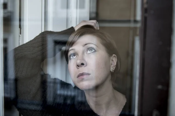 Dramatisches Nahaufnahme-Porträt einer jungen schönen Frau, die traurig ist und Depressionen am Fenster ihres Hauses erleidet und deprimiert wirkt — Stockfoto