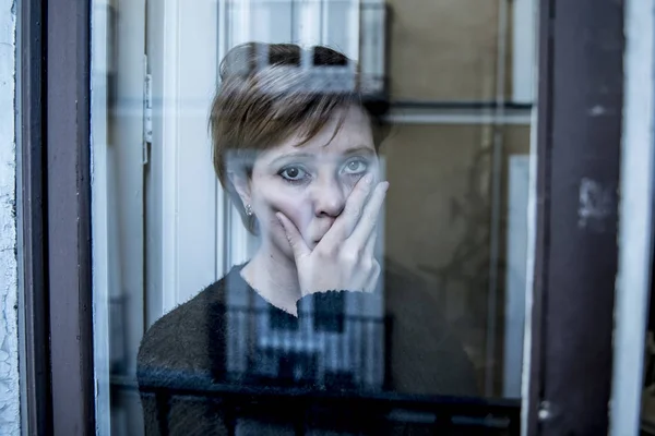 Dramatisches Nahaufnahme-Porträt einer jungen schönen Frau, die traurig ist und Depressionen am Fenster ihres Hauses erleidet und deprimiert wirkt — Stockfoto