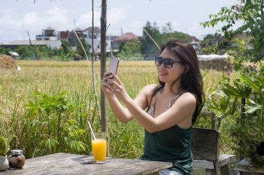 20'li veya sahip gülümseyen 30s mutlu Asyalı Çinli kadın selfie PIC pirinç alan café olması, cep telefonu ile portakal suyu alarak eğlenceli