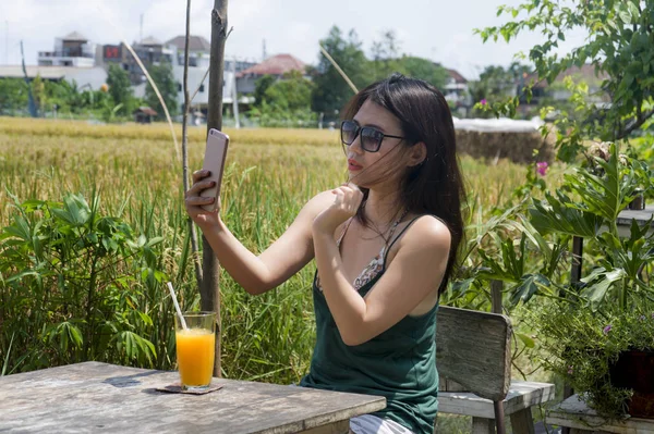 Ázsiai kínai nő, ő 20-as vagy 30-as mosolyogva, miután a móka az interneten keresztül mobiltelefon lövöldözős selfie vagy csevegnek, narancslevet ivott — Stock Fotó