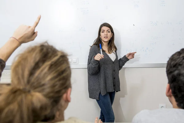 Gruppe junger Studenten nimmt Unterricht im Hörsaal der Universität, wobei Mädchen an der Tafel stehen und Schüler am Schreibtisch sitzen — Stockfoto