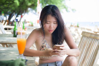 güzel Asyalı Çinli kadın yaz tatili zevk plaj restoran Resort'ta oturan cep telefonunda internet sosyal medya kullanarak 