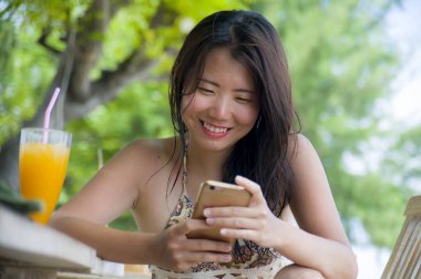 güzel Asyalı Çinli kadın yaz tatili zevk plaj restoran Resort'ta oturan cep telefonunda internet sosyal medya kullanarak 