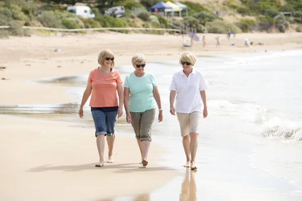 Группа из трех пожилых зрелых женщин в возрасте 60 лет, веселящихся вместе, счастливо гуляющих по пляжу, улыбающихся игриво — стоковое фото