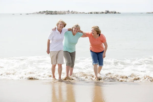 Ομάδα των τριών ανωτέρων ώριμη συνταξιούχος γυναικών σε 60 τους διασκεδάζοντας απολαμβάνοντας μαζί ευτυχισμένη περπάτημα στην παραλία χαμογελώντας παιχνιδιάρικο — Φωτογραφία Αρχείου