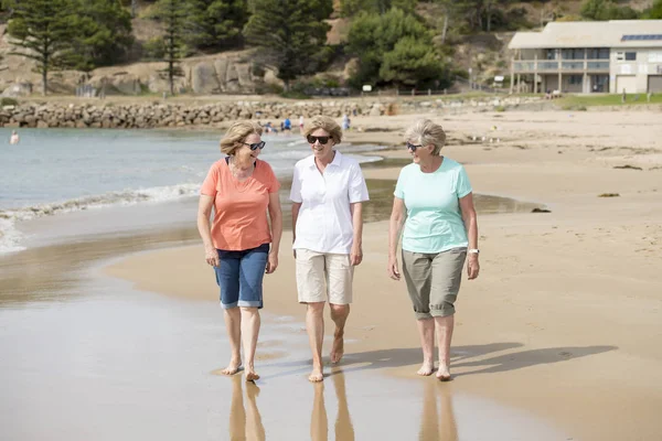 Группа из трех пожилых зрелых женщин в возрасте 60 лет, веселящихся вместе, счастливо гуляющих по пляжу, улыбающихся игриво — стоковое фото