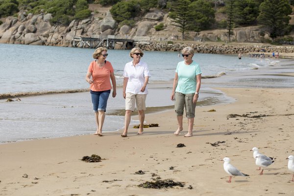 группа из трех пожилых зрелых женщин в возрасте 60 лет, веселящихся вместе, счастливо гуляющих по пляжу, улыбающихся игриво
