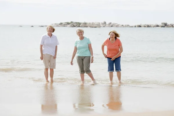 Group of three senior mature retired women on their 60s having fun enjoying together happy walking on the beach smiling playful — Stock Photo, Image